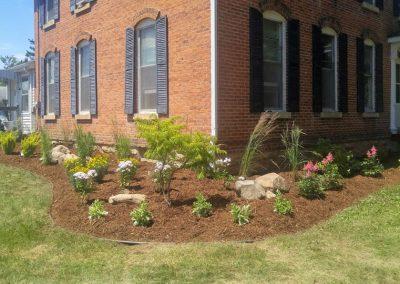 A before and after photo showing the results of Black Brook employees creating a large landscape bed and installing new shrubs and plants.