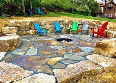 A custom fire pit surrounded by multi colored lawn chairs.