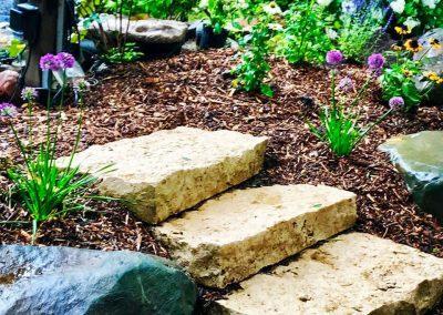 Natural stone steps surrounded by a landscape bed filled with purple flowers and brown mulch
