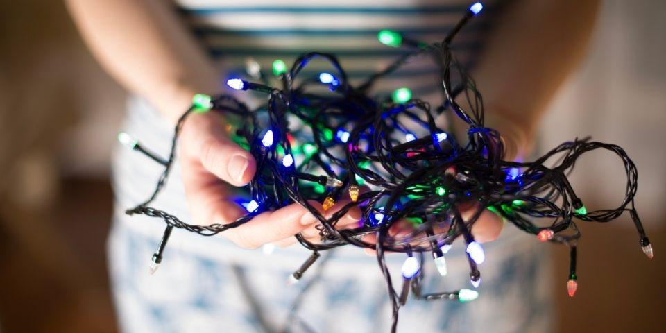 A woman holding a bundle of tangled multicolored Christmas lights.