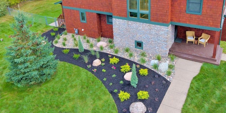 A large landscape bed filled with fresh black mulch, small shrubs and bushes, and decorative rocks.